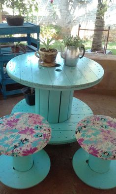 an outdoor table with two stools on it and a potted plant in the background