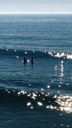 two people in the ocean on surfboards with sun reflecting off their backs and back