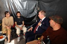 four people sitting in chairs talking to each other and one person standing up with his hand on his hip