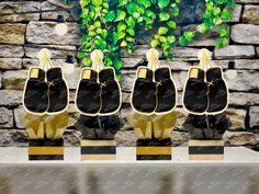 three black and gold shoes are on display in front of a stone wall with ivy