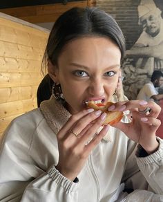 a woman in white jacket eating a doughnut with toppings on top of it