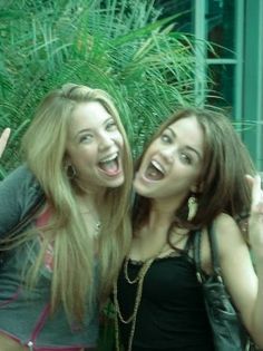 two young women standing next to each other and making the peace sign with their hands