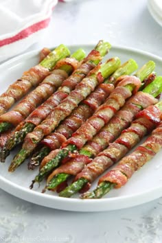 asparagus wrapped in bacon on a white plate with other food items around it