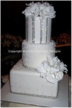 a wedding cake with white flowers and diaper on the bottom tier is decorated with silver sequins