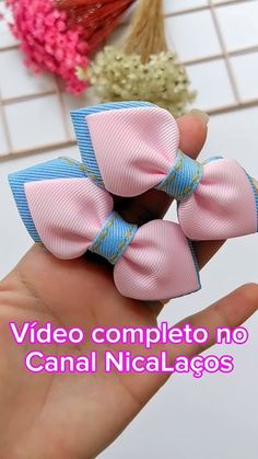 small pink and blue bow hair clip on someone's hand with flowers in the background