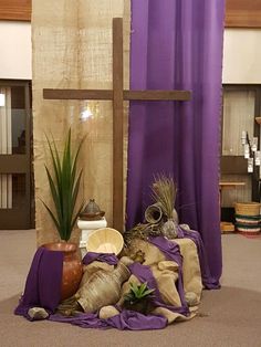 a cross, potted plants and other items are on the floor in front of a purple curtain