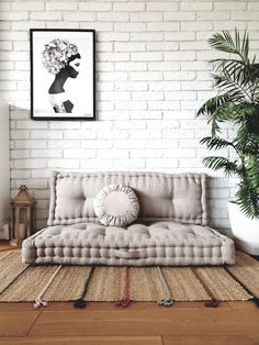 a living room with a couch, rug and potted plant on the floor in front of a white brick wall