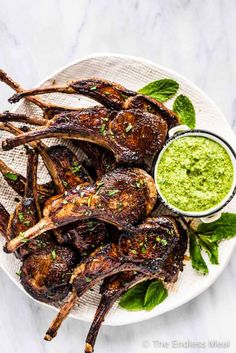 grilled lamb chops on a white plate with green dipping sauce and mint leaves