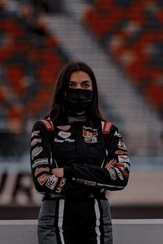 a woman wearing a face mask standing in front of a race track with her hands on her hips