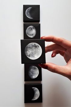 hand holding up three small black and white moon paintings on the side of a wall