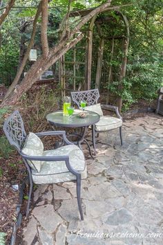 an outdoor table and chairs are set up on a stone patio with trees in the background