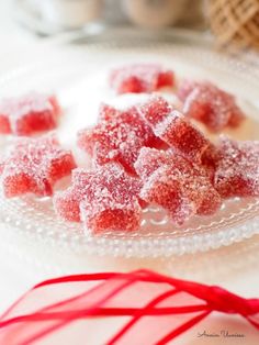 some sugar cubes are on a plate with a red ribbon around it and two cups in the background