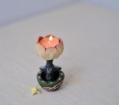 a small ceramic candle holder with a single lit candle in it's center on a white surface