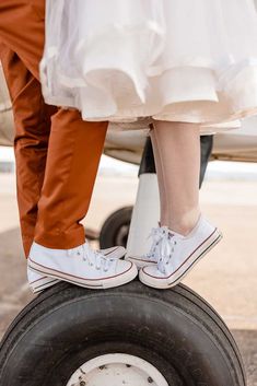 two people standing on top of an airplane tire with their feet in the air and one person wearing white tennis shoes