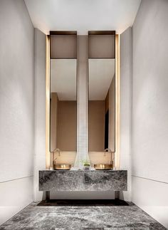 two sinks and mirrors in a bathroom with marble flooring on the walls, along with gold lights above them