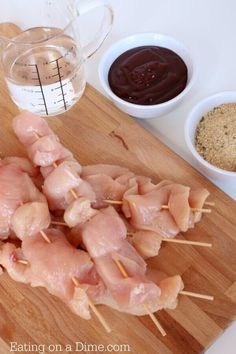 chicken skewers on a wooden cutting board next to measuring cups and sauces