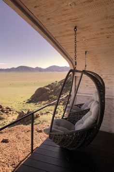 a swing chair hanging from the side of a wooden building with mountains in the background