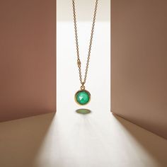 a necklace with a green stone hanging from it's center on a gold chain