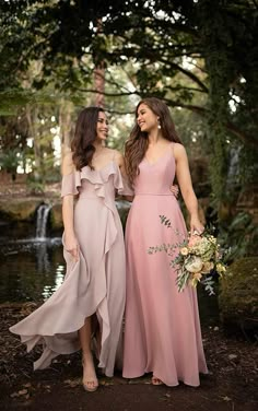 two women standing next to each other in front of a pond wearing dresses and holding bouquets