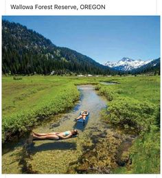 two people laying on their stomachs in the middle of a stream with mountains in the background