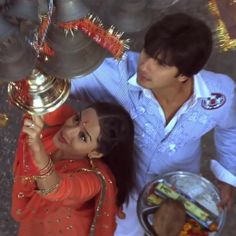 a man and woman standing next to each other in front of a metal bowl with food on it