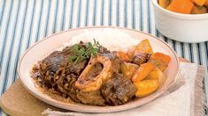 a white plate topped with meat and veggies next to a bowl of carrots