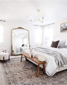 a cat sitting on a bench in front of a bed with white sheets and pillows