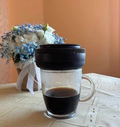 a cup of coffee sitting on top of a table next to a vase with flowers