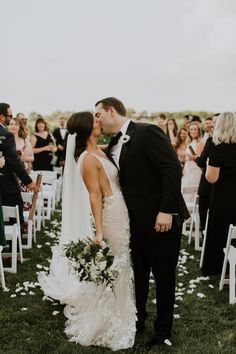 a bride and groom kissing in front of an outdoor ceremony with white petals on the grass