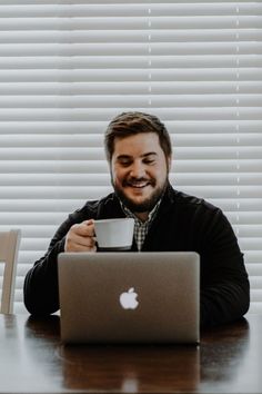 a man sitting at a table with a laptop and coffee cup in front of him