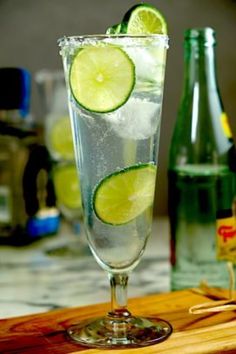 a glass filled with water and lime slices on top of a wooden cutting board next to bottles