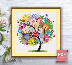 a cross stitch tree with colorful flowers on it and the frame is next to it