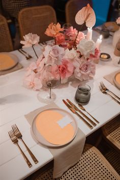 the table is set with silverware and pink flowers in vases, candles and napkins