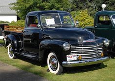 an old black pickup truck parked in the grass next to another green pick up truck