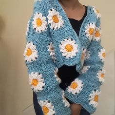 a woman wearing a blue crocheted sweater with white and yellow flowers