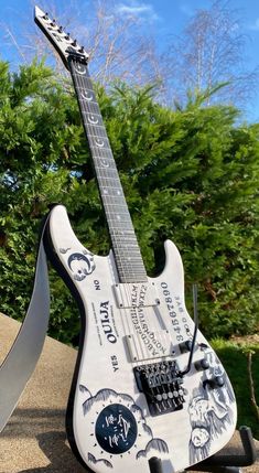 an electric guitar is on display outside in front of some bushes and trees, with a large knife sticking out of it's back end