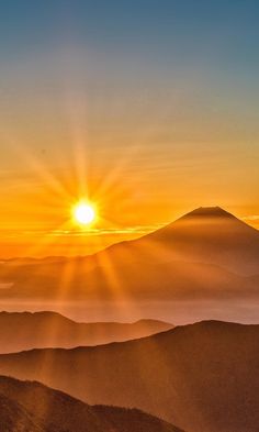 the sun is setting over mountains with mist in the foreground and fog in the background