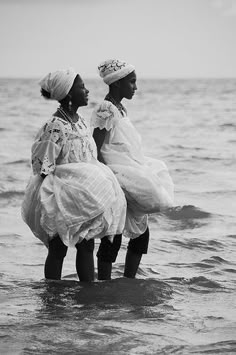 two women standing in the ocean with their backs to each other, wearing dresses and bonnets