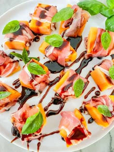 a white plate topped with slices of fruit covered in chocolate sauce and mint leafy garnish