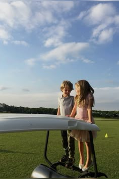 two young children standing in front of a small airplane on the grass with their arms around each other