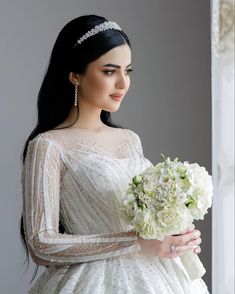 a woman in a white dress holding a bouquet of flowers and wearing a tiara