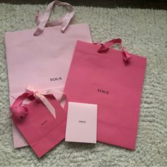 two pink shopping bags sitting on top of a white carpet next to a tag with the word tous written on it