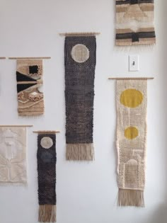 several woven wall hangings with circles and dots on them in a white walled room