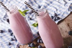 two glasses filled with blueberry smoothie on top of a cutting board