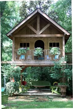 a small wooden house in the middle of some trees and grass with potted plants