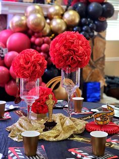 red flowers are in vases on a table with other decorations and balloons behind it