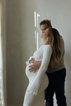 a pregnant woman standing in front of a window with her hands on the belly of a man