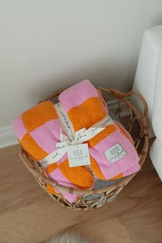 two towels wrapped in pink and orange are sitting on a wicker basket next to a white cat