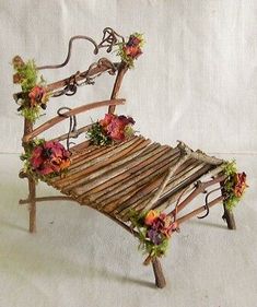 a miniature bench made out of branches with flowers on the top and bottom, sitting against a white background