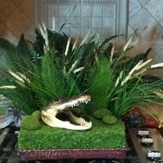 there is a fake alligator head in the center of this planter with artificial grass